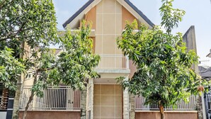 A two-story house with a balcony, a gated entrance, and a small garden area with trees and plants. - SPOT ON 92916 Batu Mas Homestay Syariah (Jogoroto)