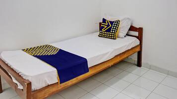 Een eenpersoonsbed met houten frame, wit beddengoed en een deken met blauw-geel patroon.