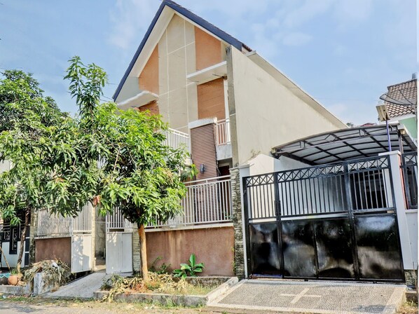 Un edificio residencial moderno de dos pisos con techo plano, entrada con portón y un pequeño balcón.