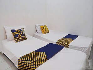Dos camas individuales con ropa de cama blanca y mantas de lunares azules y amarillos.