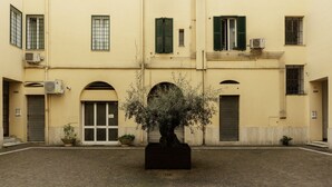 Une cour intérieure avec un jardinière centrale, un bâtiment doté d’entrées en arc de cercle et d’un sol carrelé.