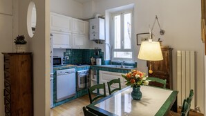 Une cuisine avec des meubles blancs, un pare-feu turquoise, une table à manger avec des chaises et une lampe suspendue.