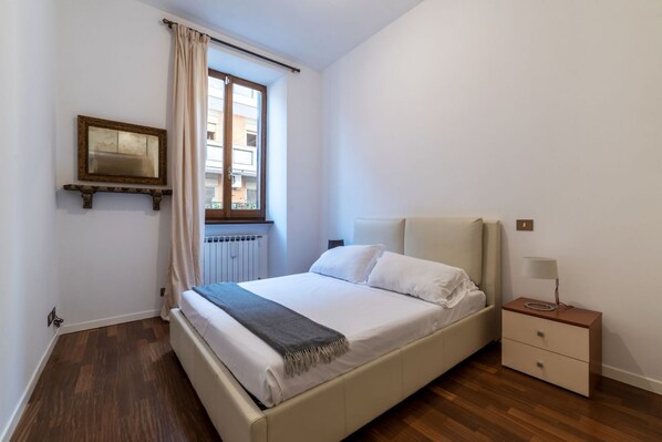 Ein Schlafzimmer mit Bett, Nachttisch, Spiegel und einem Fenster mit Vorhängen.