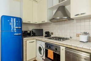 A compact kitchen with a blue refrigerator, a microwave, a gas stove, a washing machine, and a dishwasher. - A stone’s throw from the Colosseum! (Roma)