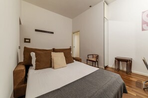 A bedroom with a bed, a chair, a small table, and a wardrobe.