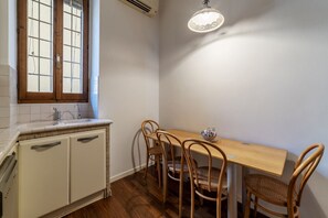 A kitchen with a wooden table and chairs, a window with blinds, and a hanging light fixture. - A stone’s throw from the Colosseum! (Roma)