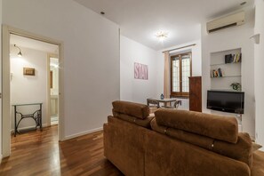 Ein Wohnzimmer mit einem braunen Sofa, einem Esstisch und einem an der Wand befestigten Fernseher.