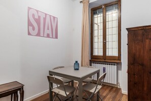 Ein Zimmer mit Tisch, Stühlen, einem Fenster mit Vorhängen und einem Heizkörper.