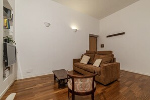 A living room with a brown sofa, a wooden coffee table, and a patterned armchair. - A stone’s throw from the Colosseum! (Roma)