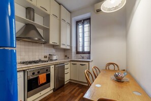 A compact kitchen with white cabinets, a gas stove, a dishwasher, and a wooden dining table with chairs.