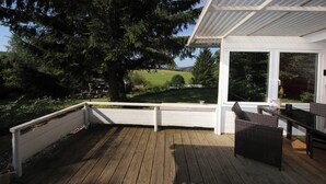 A wooden deck with a white railing, a wicker chair, and a table. - Vacation home Beerberg, cozy vacation home at the biosphere reserve Thuringian Forest (Suhl)