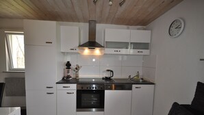 A modern kitchen with white cabinetry, stainless steel appliances, and a wooden ceiling. - Vacation home Beerberg, cozy vacation home at the biosphere reserve Thuringian Forest (Suhl)