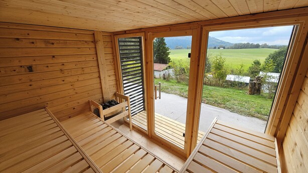 A wooden cabin with a loft bed, a small wooden bench, and a sliding door leading to an outdoor area. - Vacation home Beerberg, cozy vacation home at the biosphere reserve Thuringian Forest (Suhl)