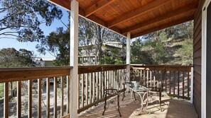 Enjoy a peaceful moment on this outdoor deck with a glass table and two chairs, surrounded by lush trees and a scenic view.