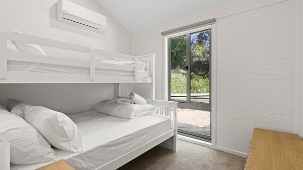 A bedroom with a bunk bed, a single bed, and a large sliding glass door leading to an outdoor area. - Treetop | Metung Nature Escape (Metung)