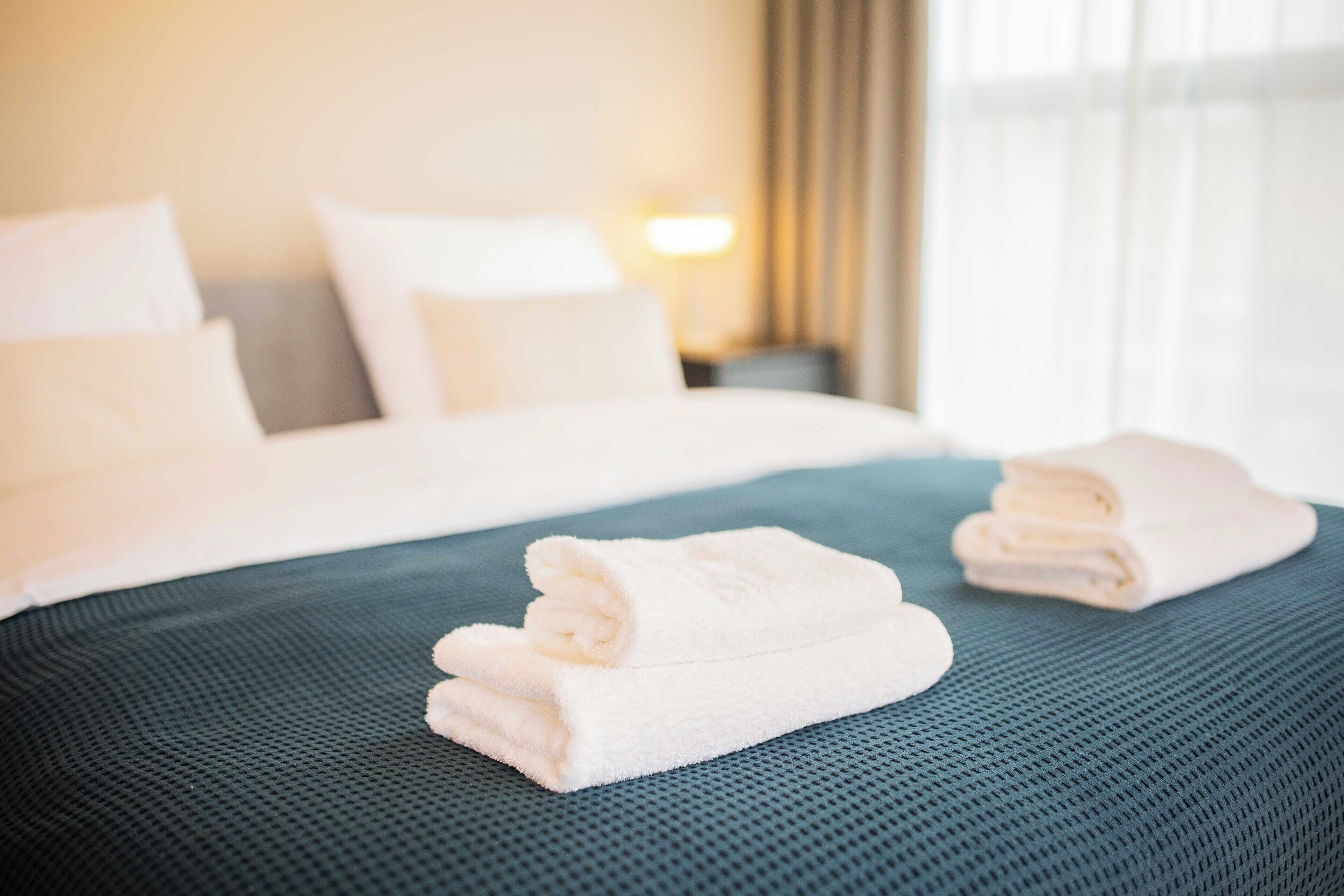 A neatly made bed with white linens and a teal bedspread in a hotel room.