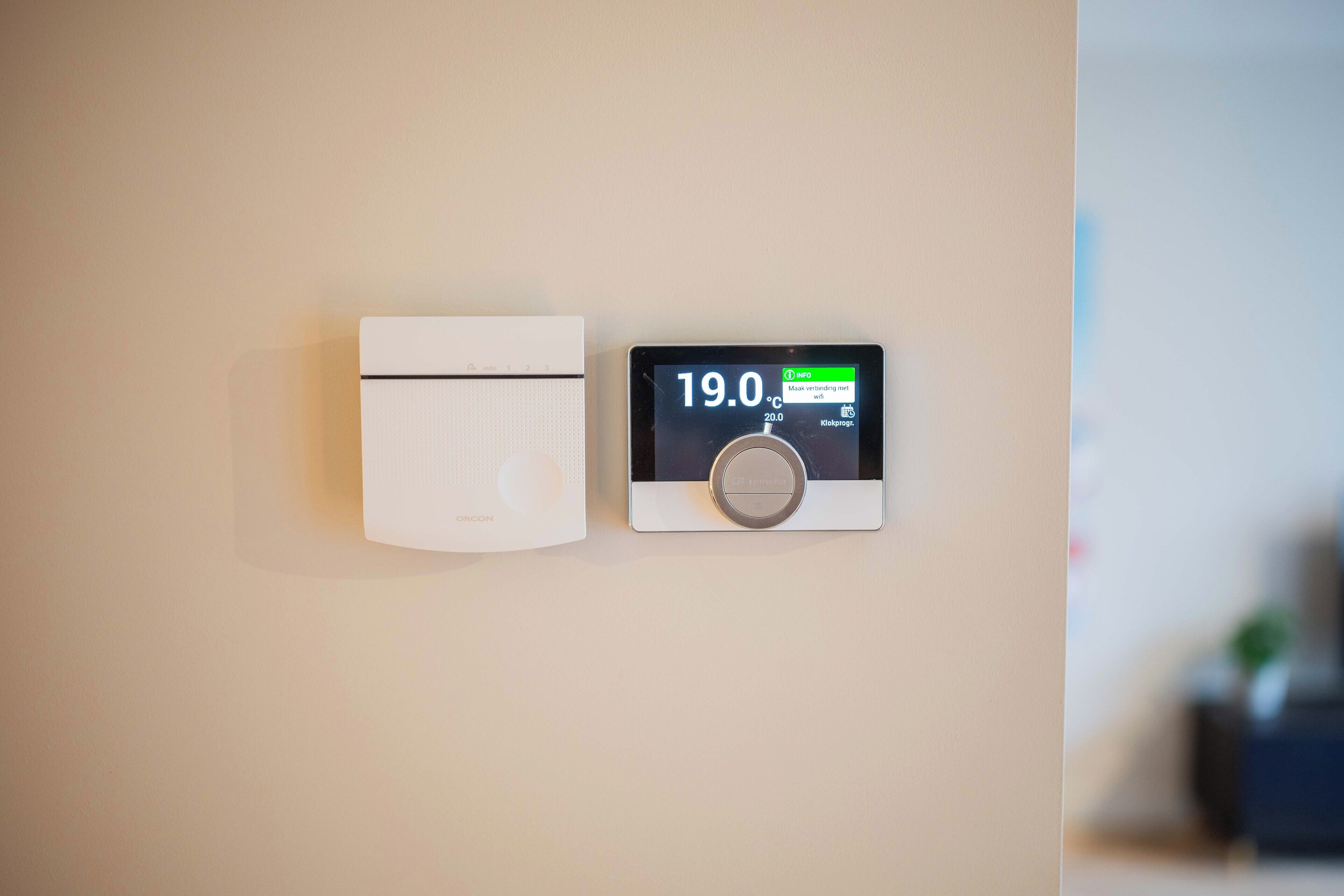 Ein Thermostat und ein an der Wand befestigtes Gerät, vermutlich ein Rauchmelder, an einer schlichten Wand.