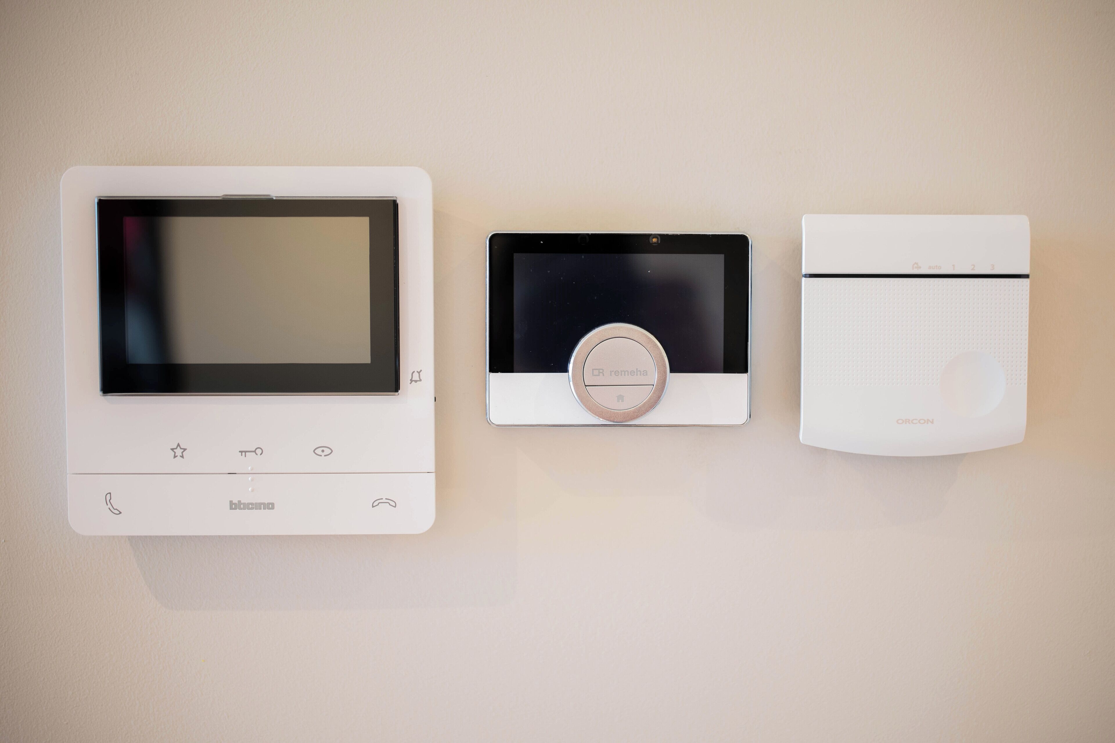 Three wall-mounted devices: a control panel with a screen, a thermostat, and a security camera.