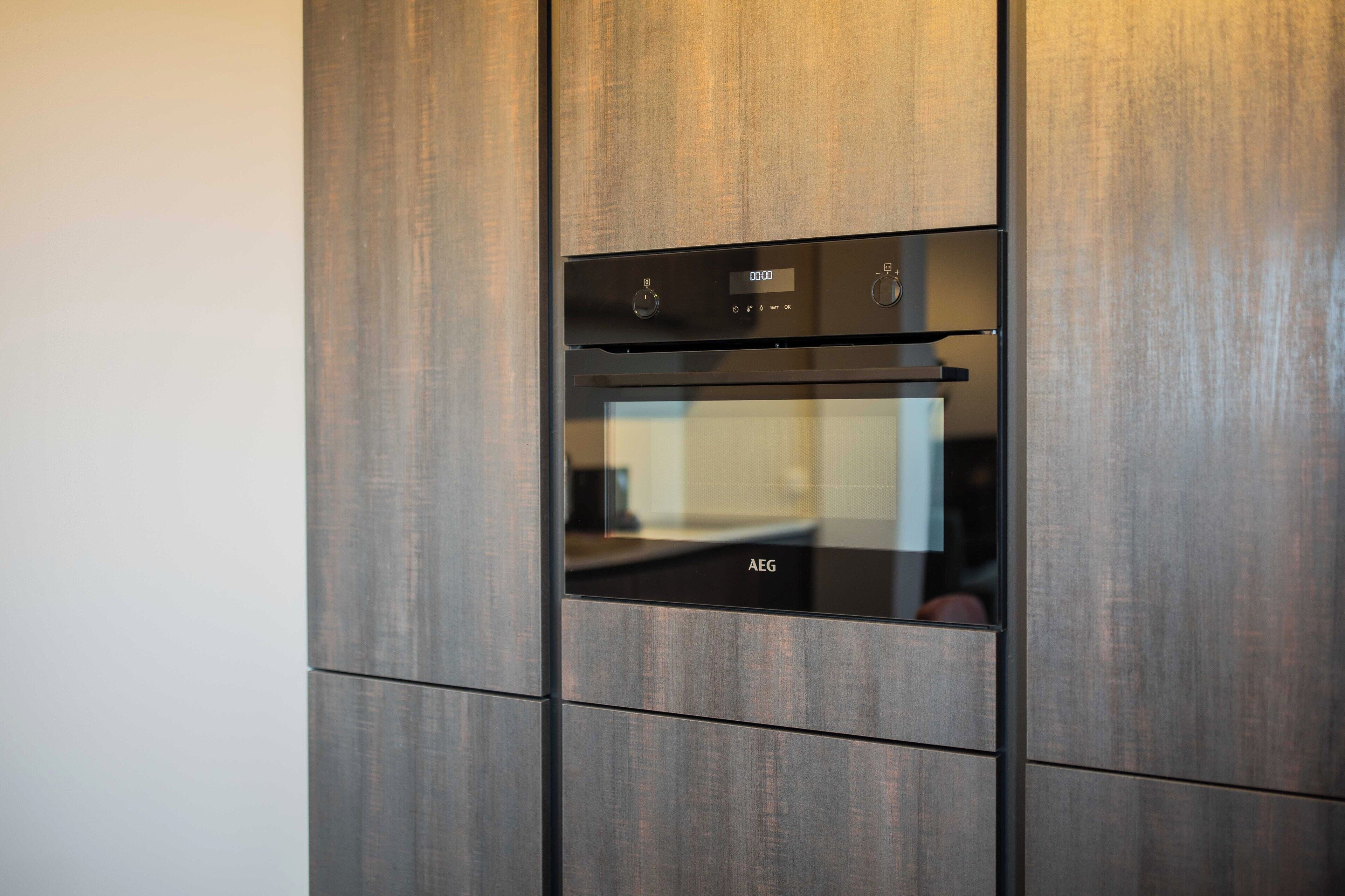 A modern kitchen with a built-in oven and microwave, featuring a sleek, dark wood finish.