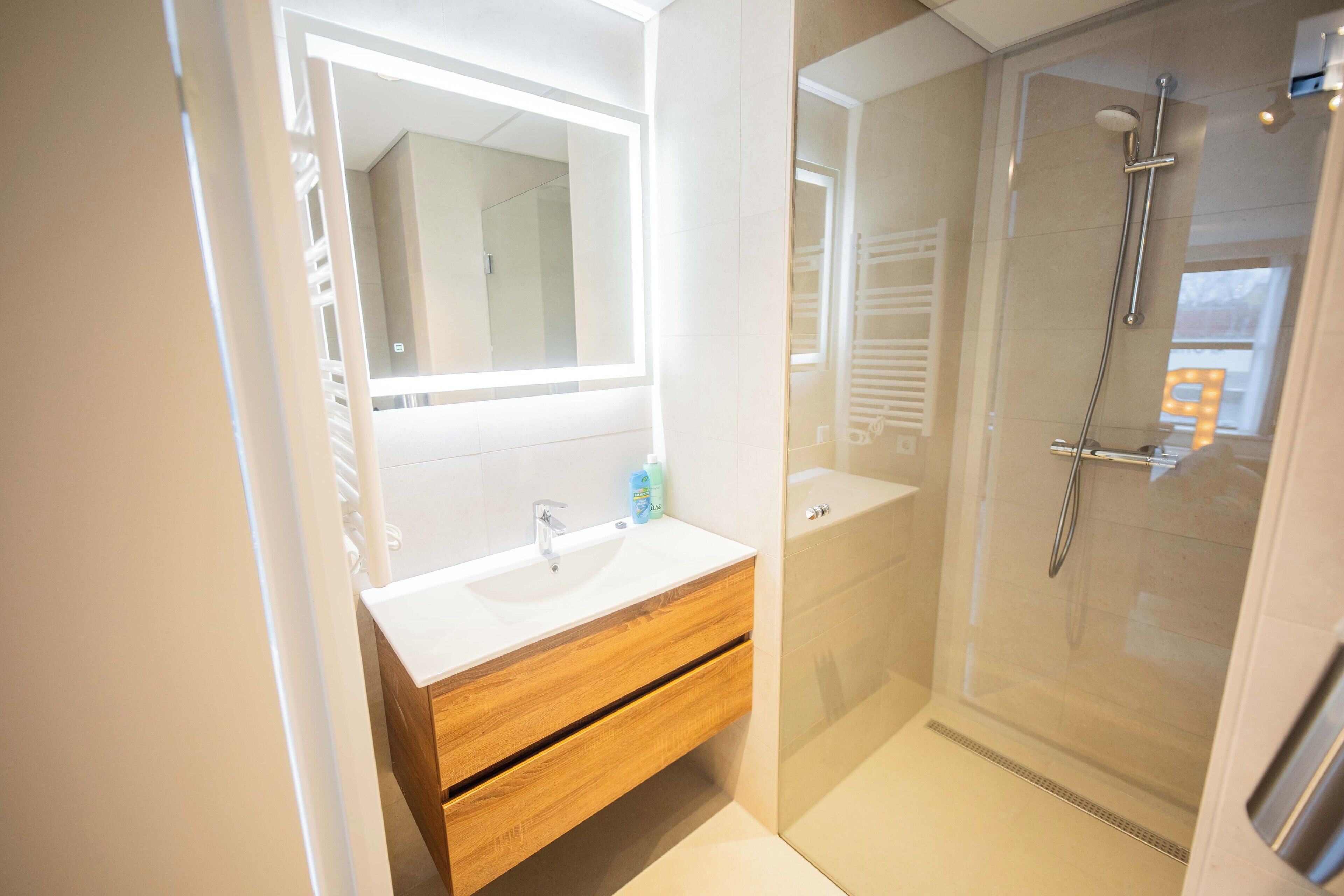 Une salle de bain moderne avec un meuble-lavabo blanc, un grand miroir et une douche à parois de verre.