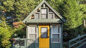 A small, single-story house with a yellow front door, green trim, and a steeply pitched roof.