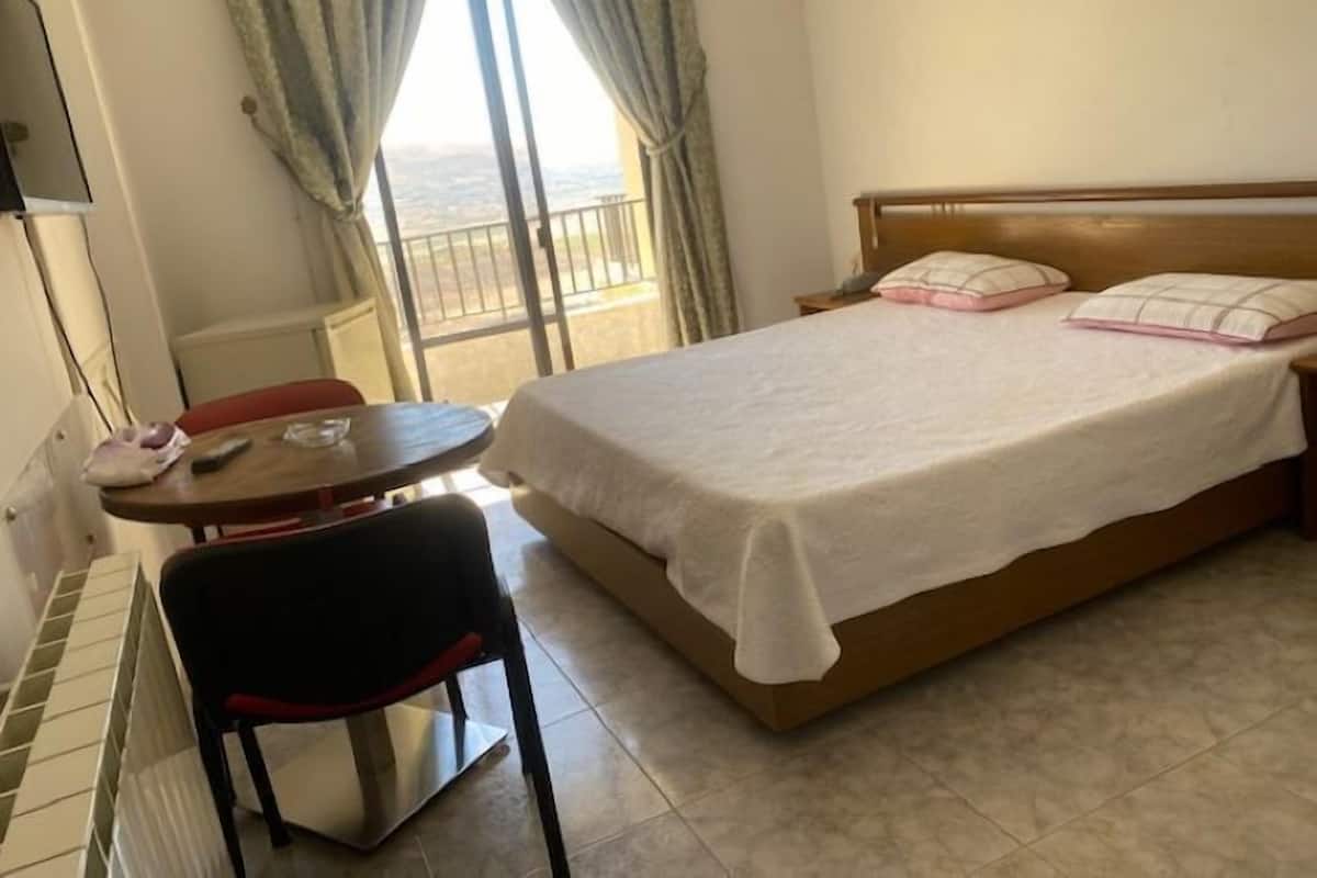 A hotel room with a bed, a table with a chair, a TV, and a view of the outdoors through a window.