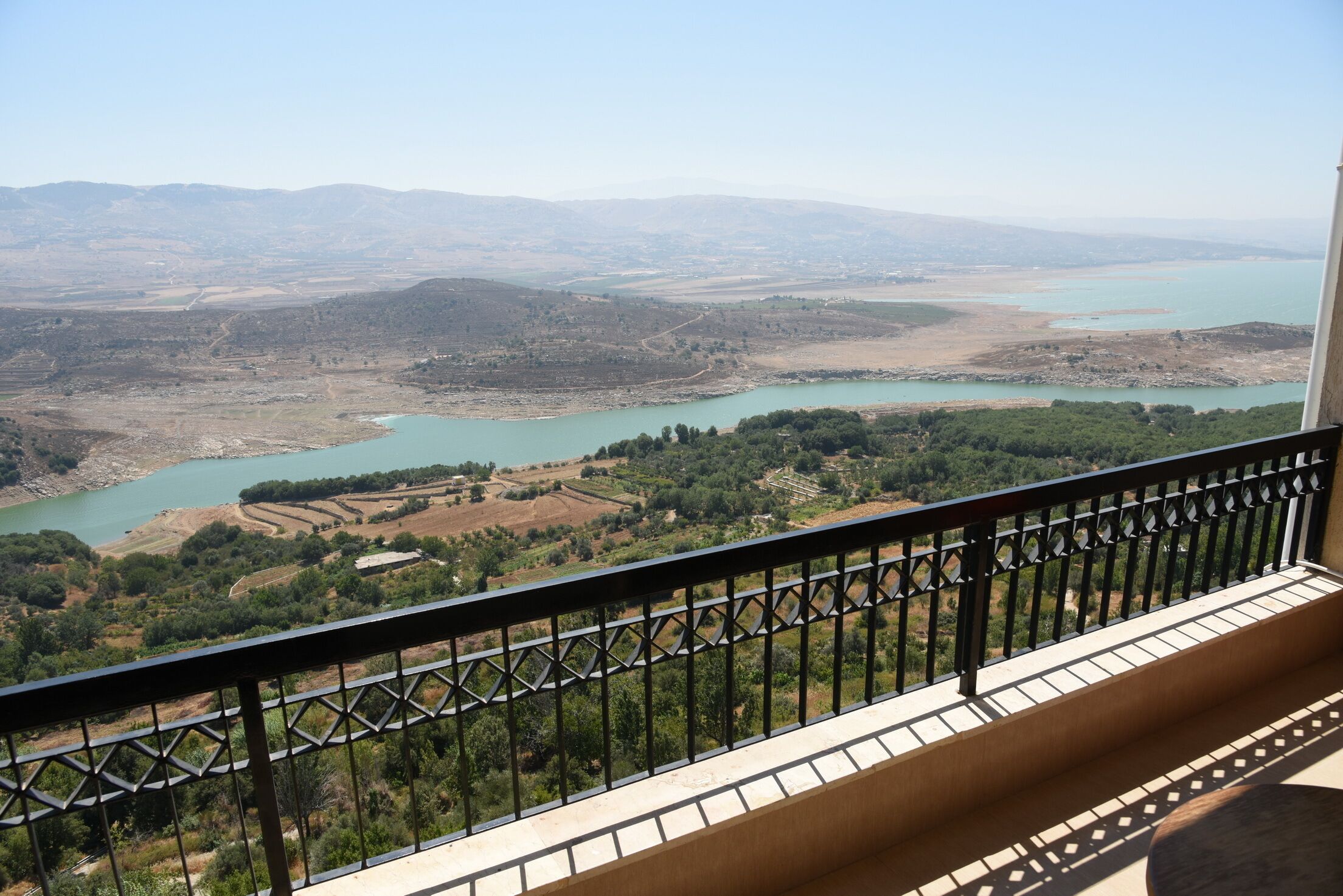 A balcony with a view of a lake and surrounding landscape.