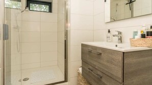 A modern bathroom with a glass-enclosed shower, a vanity with a mirror, and a small window. - Sun, sea, sand, wind, marram grass – this 4-person chalet embodies the pure beach feeling from your (Burgh-Haamstede)