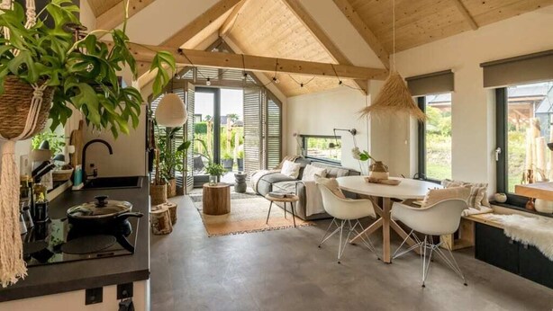 A spacious kitchen with a dining area, wooden ceiling beams, and large windows. - Sun, sea, sand, wind, marram grass – this 4-person chalet embodies the pure beach feeling from your (Burgh-Haamstede)