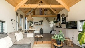 A modern living room with a high ceiling, wooden beams, a grey sofa, a coffee table, and a television. - Sun, sea, sand, wind, marram grass – this 4-person chalet embodies the pure beach feeling from your (Burgh-Haamstede)