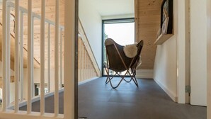 Un intérieur en bois avec une chaise posée sur un plancher sombre, une rambarde blanche et une porte donnant sur un espace extérieur.