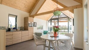 Une cuisine moderne avec des meubles en bois, un coin repas doté de chaises en osier blanc et une grande fenêtre laissant entrer la lumière naturelle.