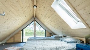 Une chambre avec un plafond en pente, un puits de lumière, un lit avec une literie bleue et une table de chevet bleue.
