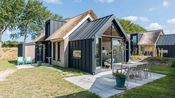 Une maison moderne avec un toit de chaume, une entrée avec une porte en verre et un patio agrémenté de mobilier d’extérieur.