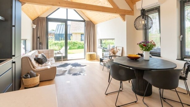 Un vaste espace de vie doté d’un haut plafond, d’une table à manger avec des chaises, d’un canapé et d’une grande fenêtre agrémentée de rideaux.