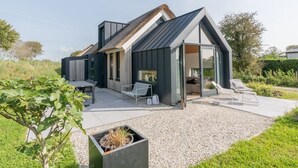 Une maison moderne avec un toit en pente, un patio avec des sièges et un jardin.
