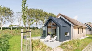 Une maison moderne avec un toit en pente, une entrée avec une porte vitrée et un patio doté d’un espace salon extérieur.