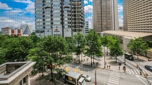 A cityscape with modern high-rise buildings, a clear sky, and a street with pedestrians and vehicles.