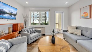 A modern living room with a grey sofa set, a wooden coffee table, and a flat-screen TV mounted on the wall.