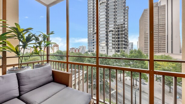 A balcony with a grey sofa, potted plants, and a view of tall buildings.