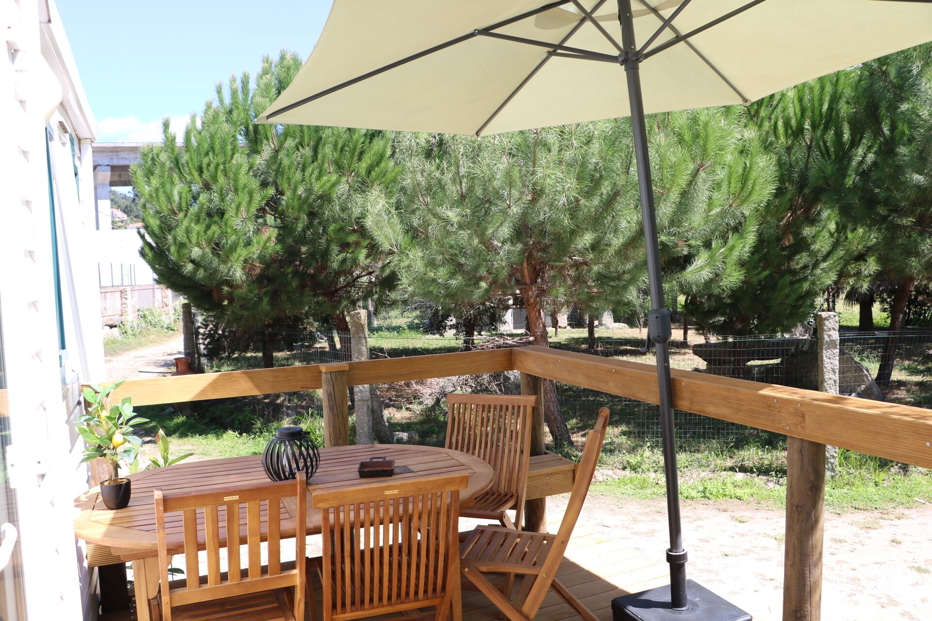 Une terrasse en bois avec une table et des chaises, un parasol et une vue sur les arbres.