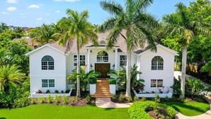 A large, white, two-story house with a symmetrical facade, a central entrance with a wooden door, and a well-maintained lawn with palm trees. - 1200 Tree Bay  (Siesta Key)