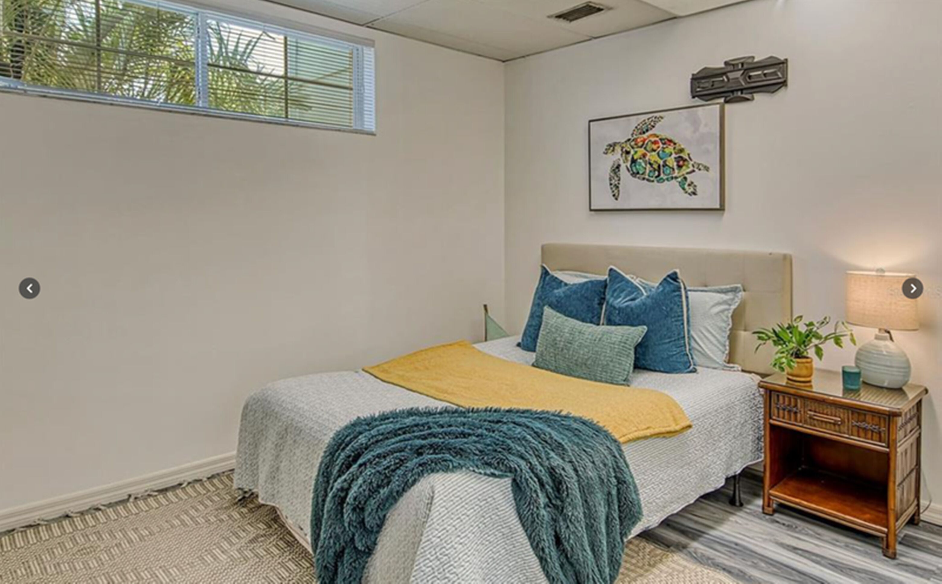 A bedroom with a bed, pillows, a bedside table with a lamp, and a framed picture on the wall.