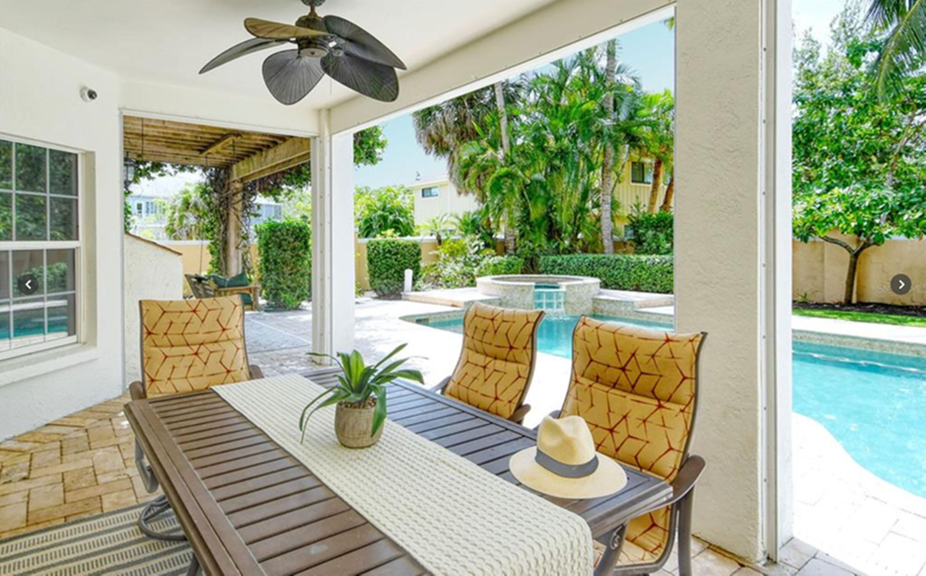 Un espacio de estar al aire libre cubierto con vistas a la piscina, que incluye una mesa, sillas y un ventilador de techo.