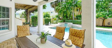 Un espacio de estar al aire libre cubierto con vistas a la piscina, que incluye una mesa, sillas y un ventilador de techo.