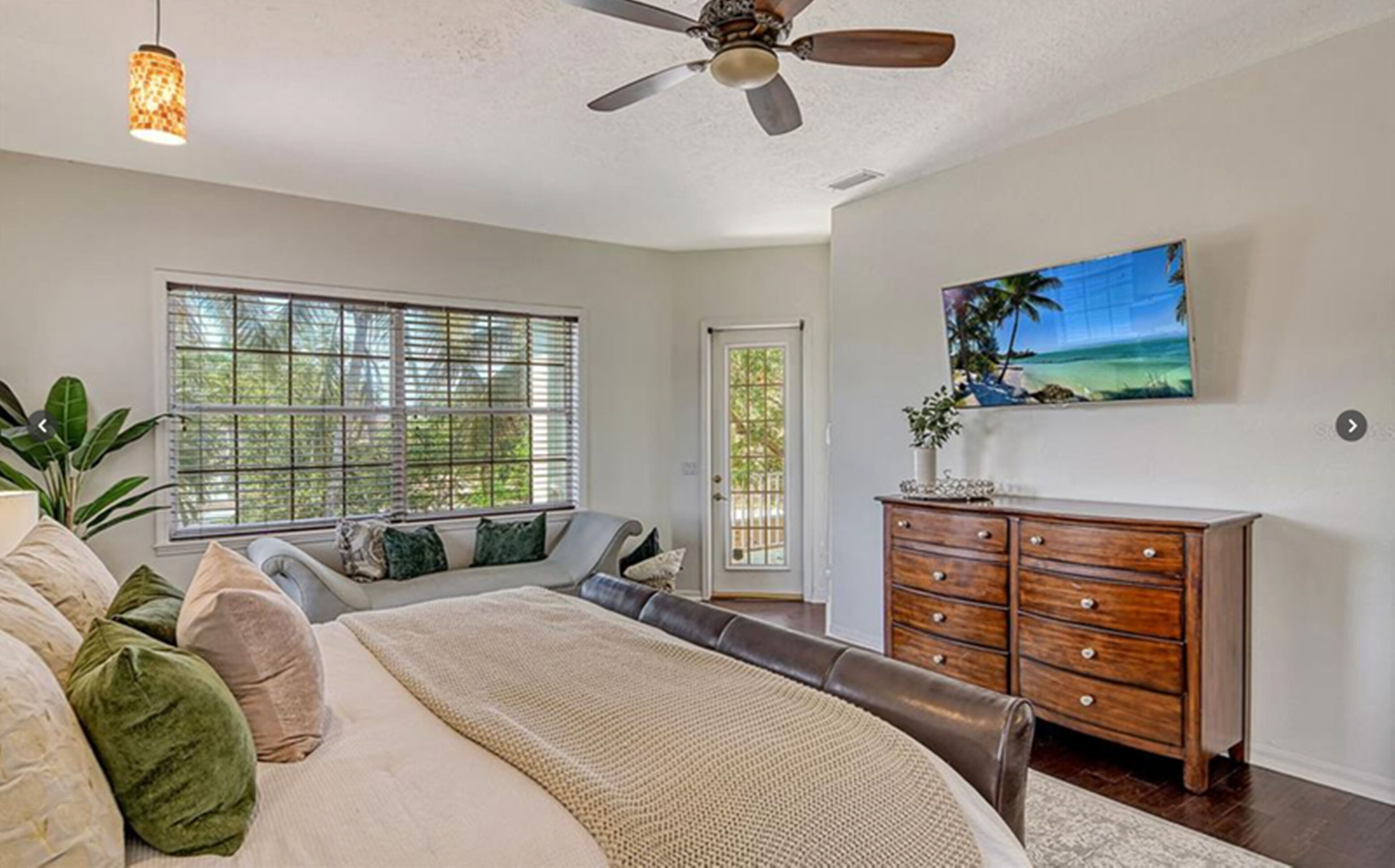 A bedroom with a bed, a dresser, a ceiling fan, a window with blinds, and a painting on the wall.