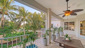 A spacious balcony with a view of palm trees and a pool, featuring a ceiling fan and potted plants. - 1200 Tree Bay  (Siesta Key)