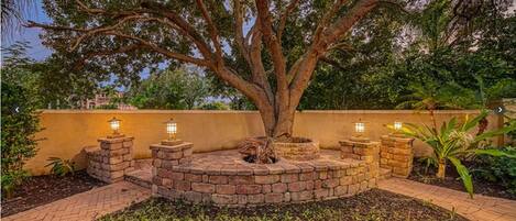 Un árbol rodeado por una jardinera de piedra circular con cuatro luces de estilo farol.