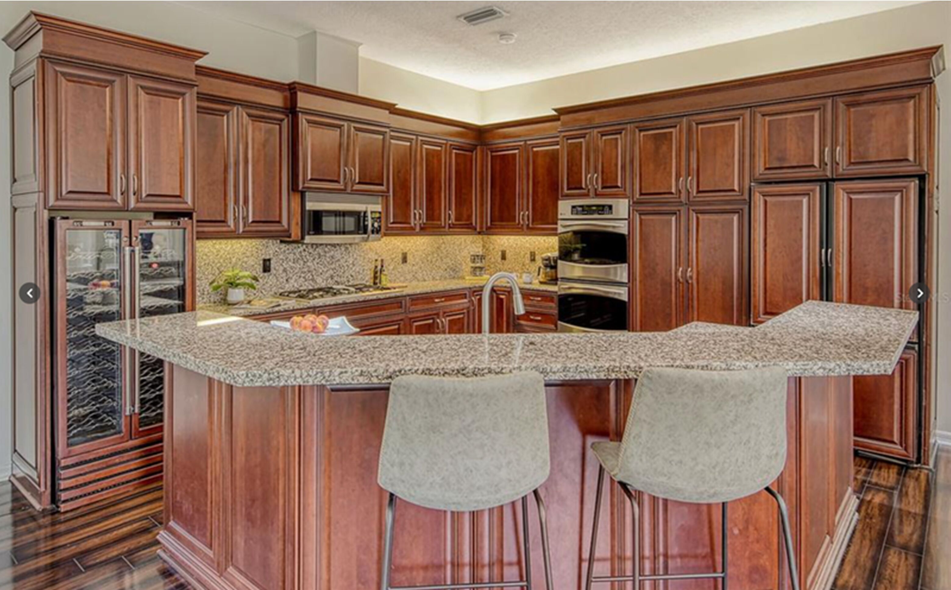A kitchen with wooden cabinets, granite countertops, stainless steel appliances, and two bar stools.