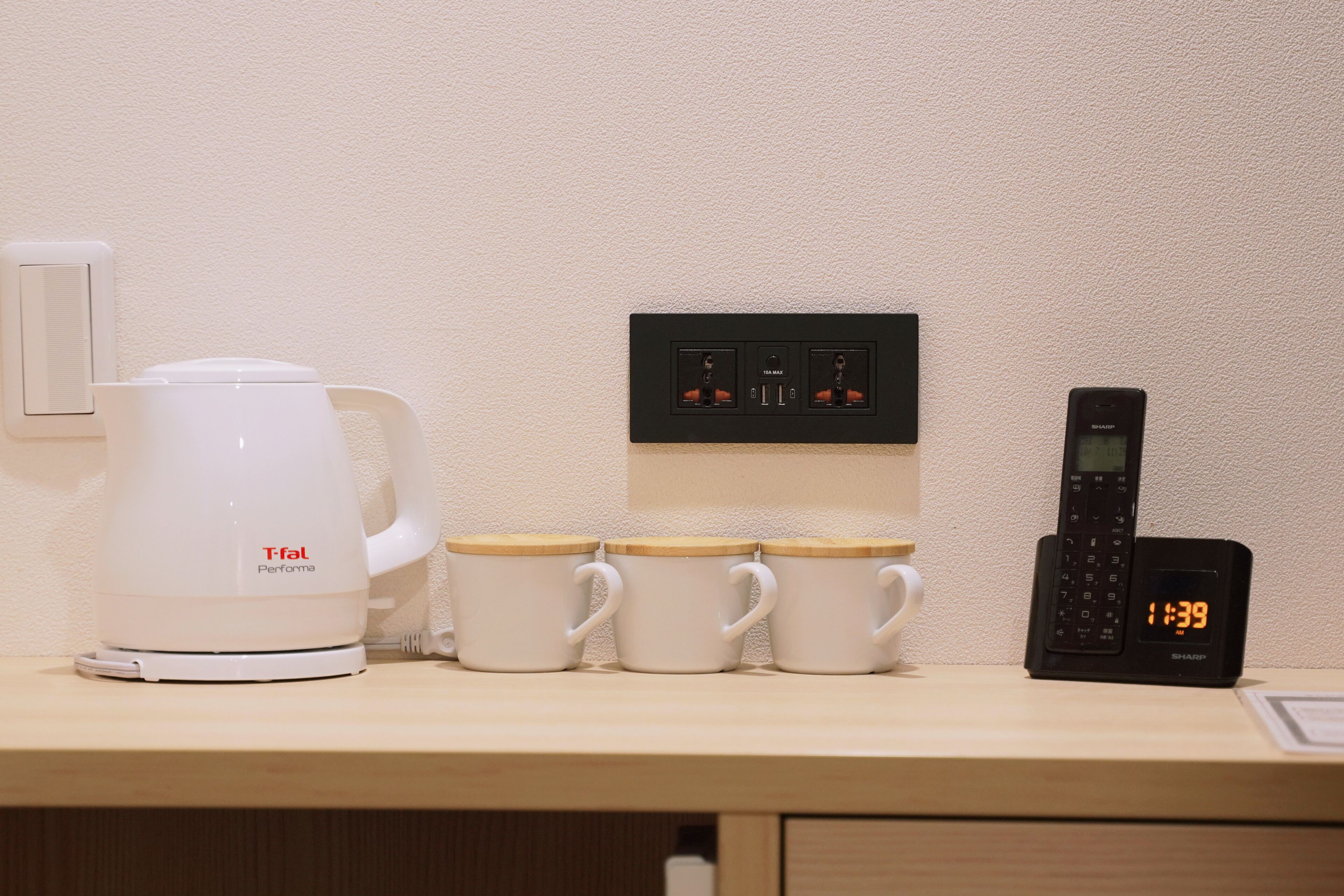 A kitchen counter with a coffee maker, three mugs, a power strip, and a phone charging station.